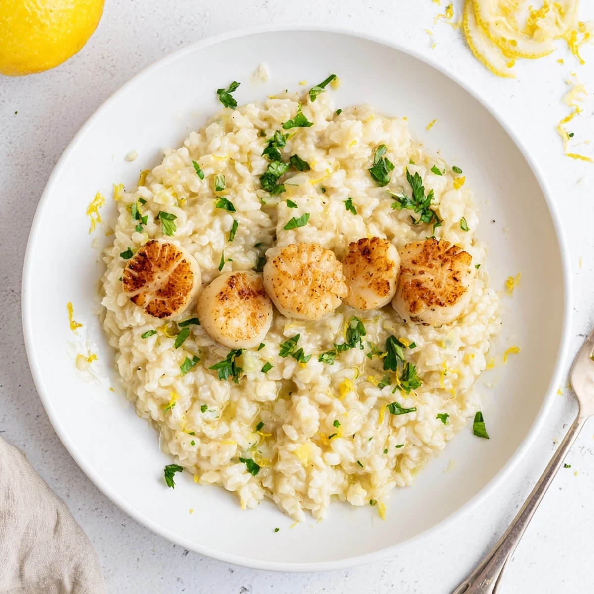 Elegant dinner plate featuring Lemon Garlic Scallops with Risotto, paired with a glass of white wine and fresh herbs.
