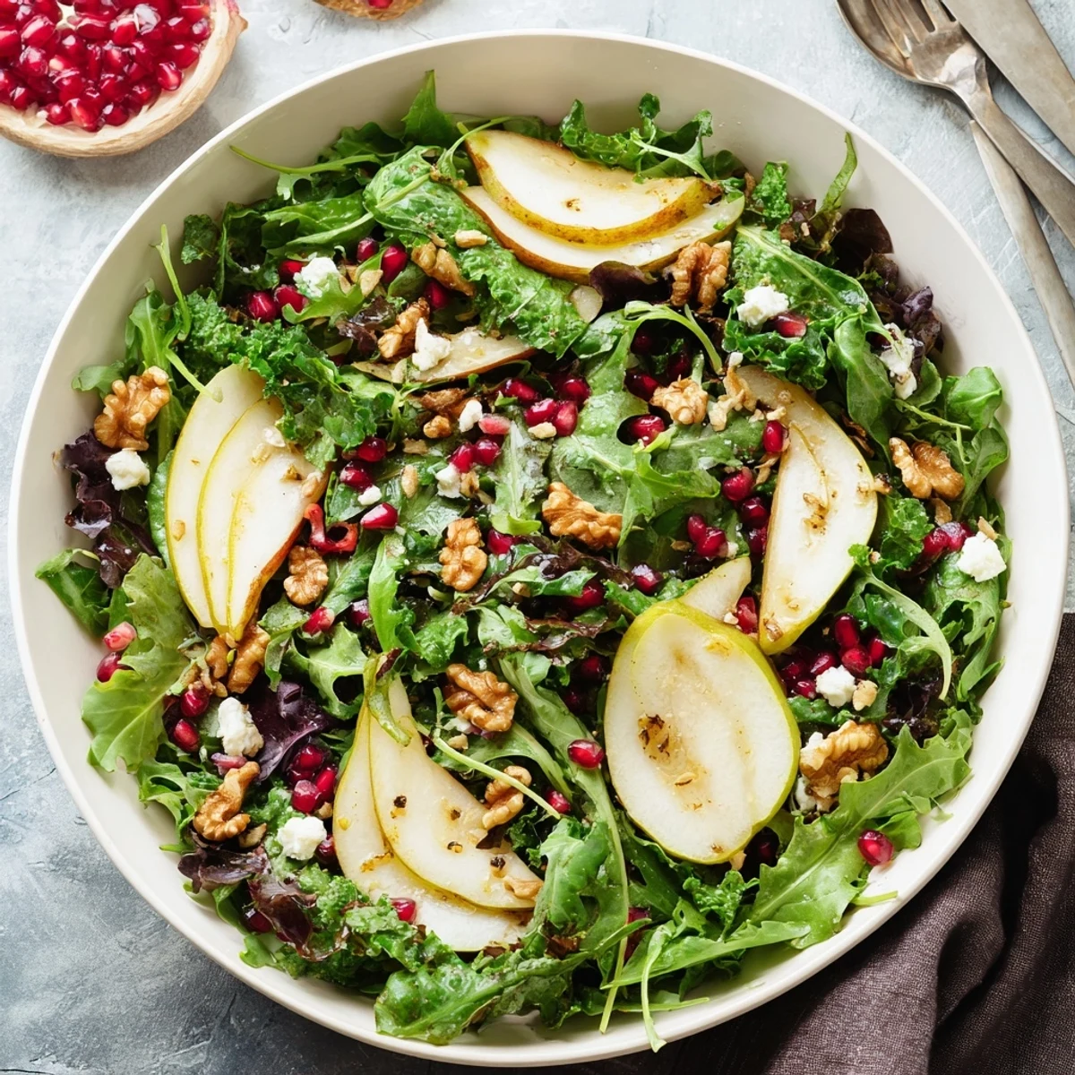 A vibrant bowl of Winter Green Salad with Pear and Walnuts, topped with crumbled goat cheese and pomegranate seeds.