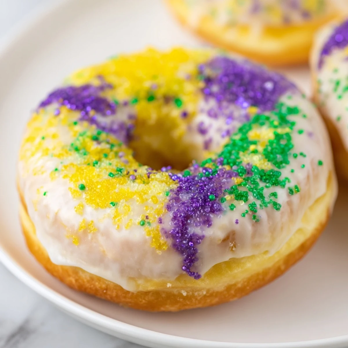 Freshly fried Mardi Gras donuts with purple, green, and yellow sugars on a wire rack.