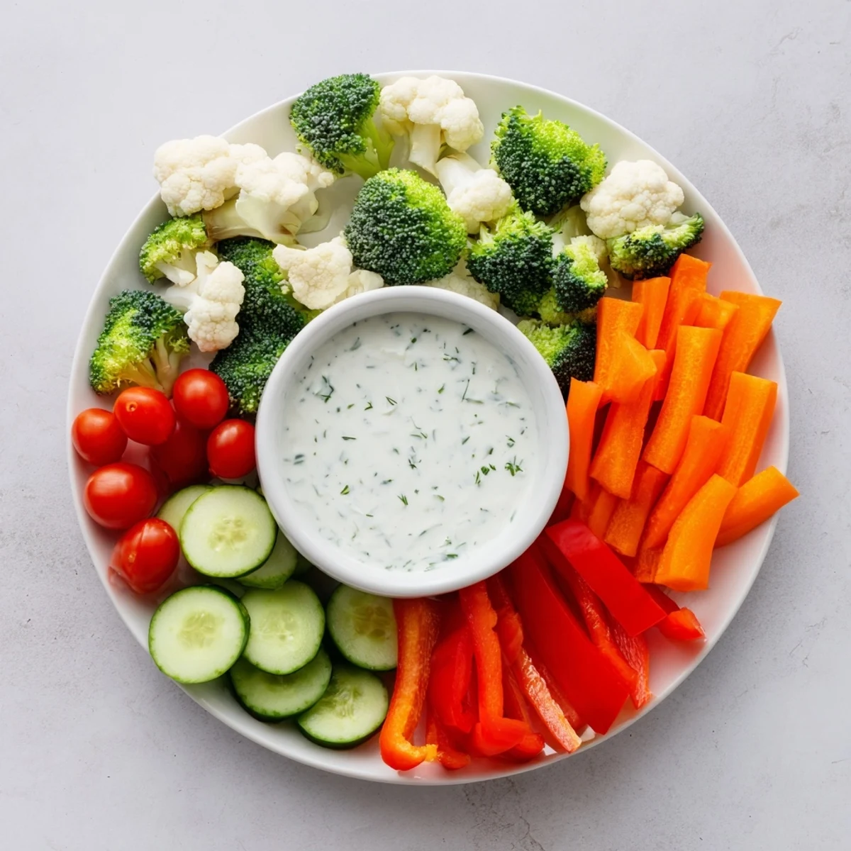 A colorful veggie tray with ranch dip features crisp carrots, cherry tomatoes, and cucumber slices, arranged for an easy appetizer.  