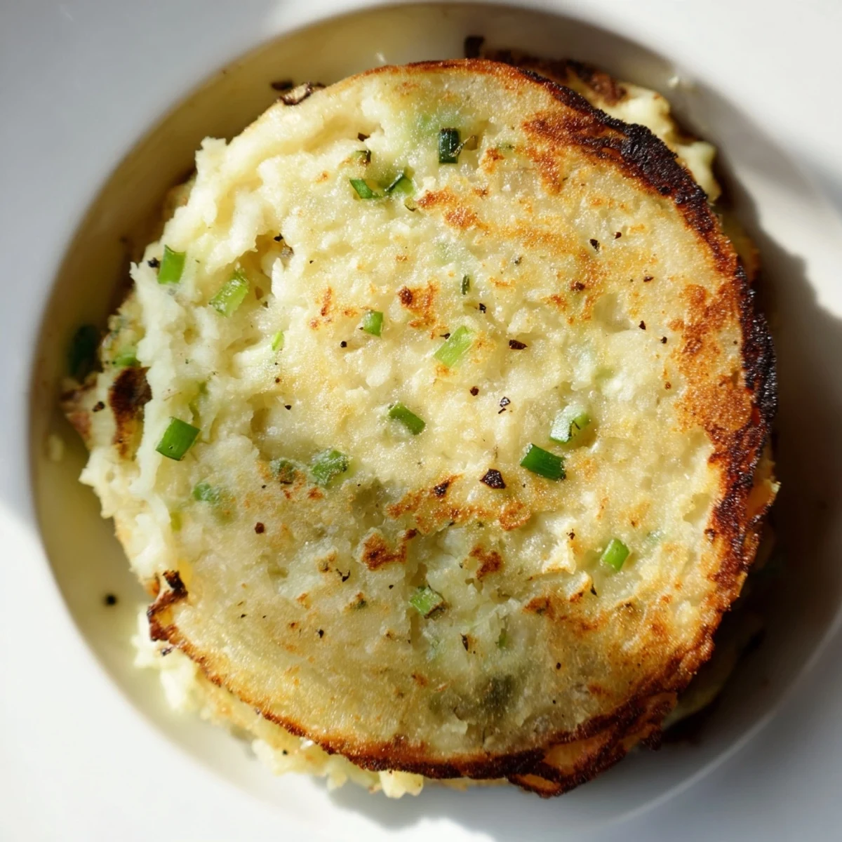 Golden-brown Irish Potato Cakes with Scallions sizzling in a skillet with fresh green onion slices visible.  