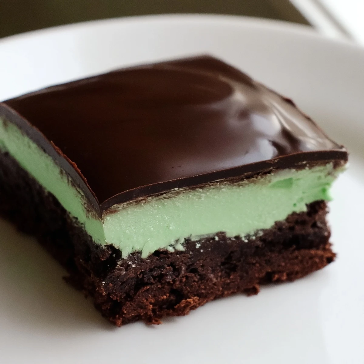 A close-up of Green Mint Brownies reveals moist texture, minty aroma, and shiny chocolate ganache topping.