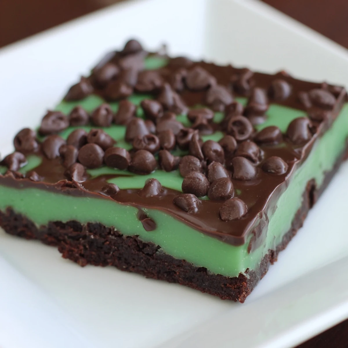 A close-up of mint brownies with chocolate chips, showing their moist crumb and glossy chocolate topping.  