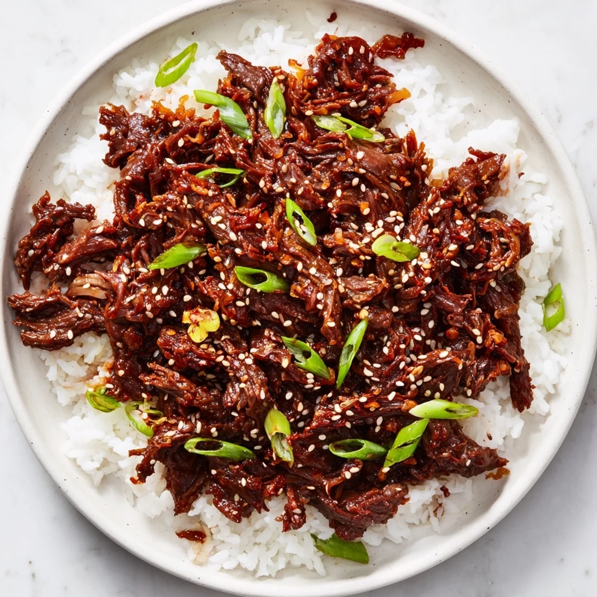 Slow cooker Korean beef piled high with tender shredded meat and fresh green onion garnish over steamed rice.