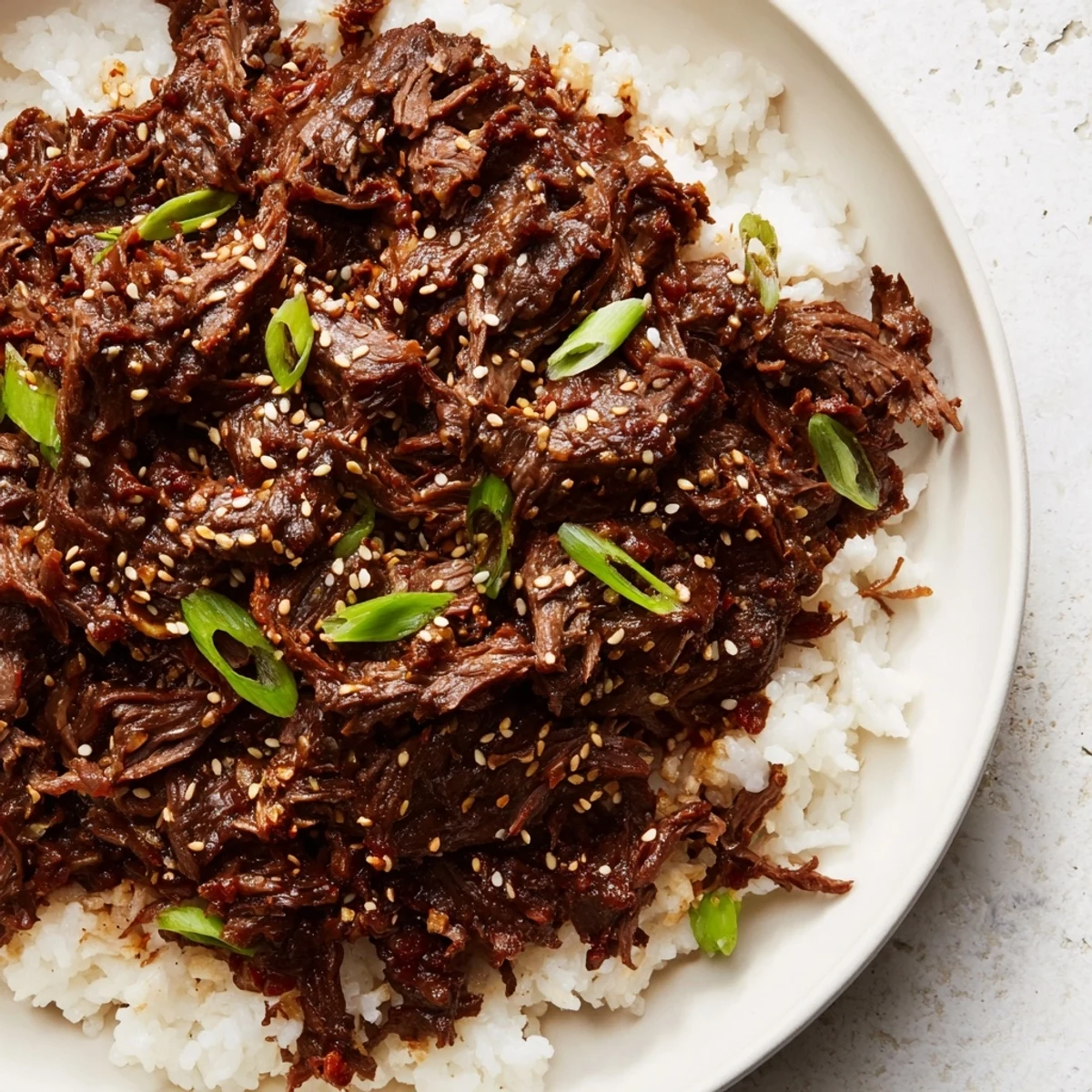 A close-up of slow cooker Korean beef in a bowl with sesame seeds and a side of kimchi.