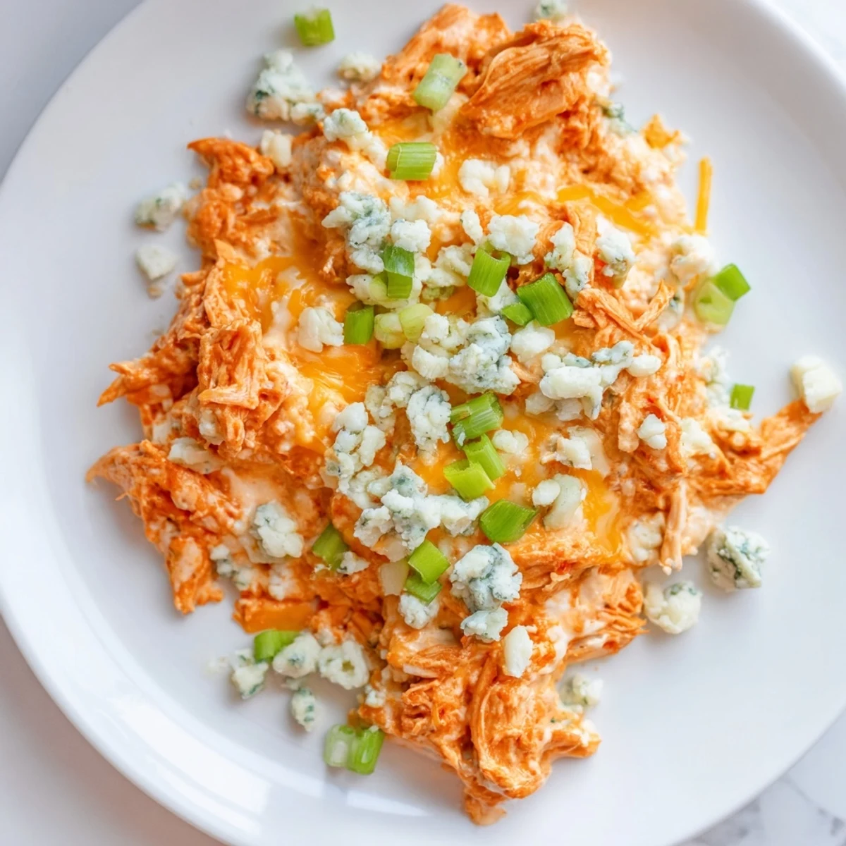 Freshly baked Keto Buffalo Chicken Dip in a baking dish, garnished with green onions and a drizzle of buffalo sauce.  