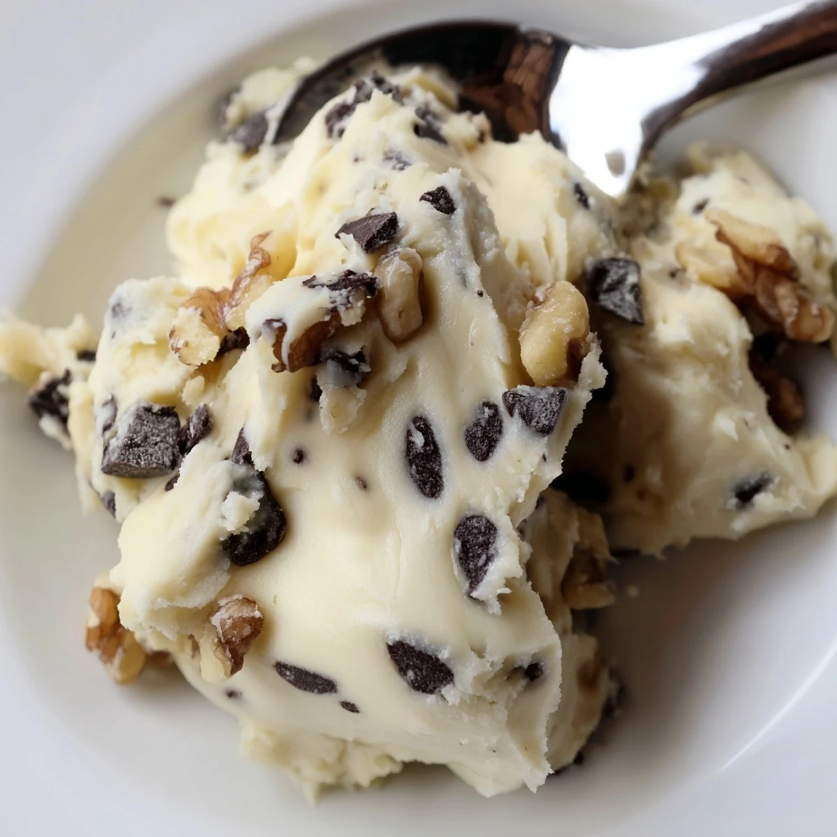 A spoon dipping into chilled Guilt Free Greek Yogurt Cookie Dough, with walnut pieces and a honey drizzle.