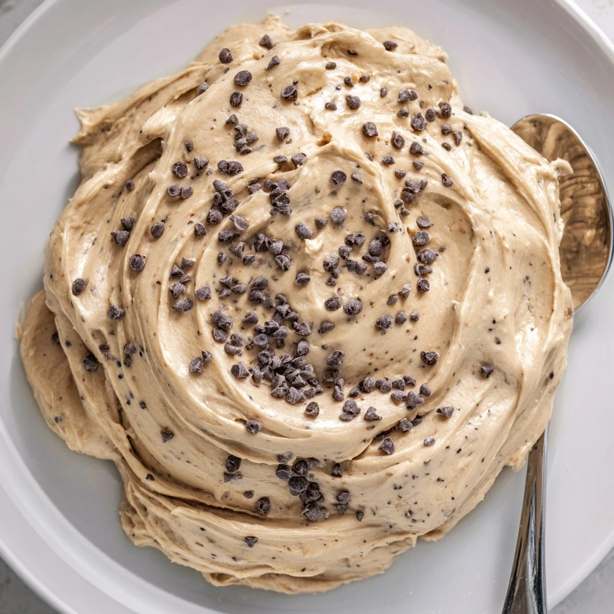 A bowl of creamy Cookie Dough Frosting with mini chocolate chips spread for frosting cupcakes.
