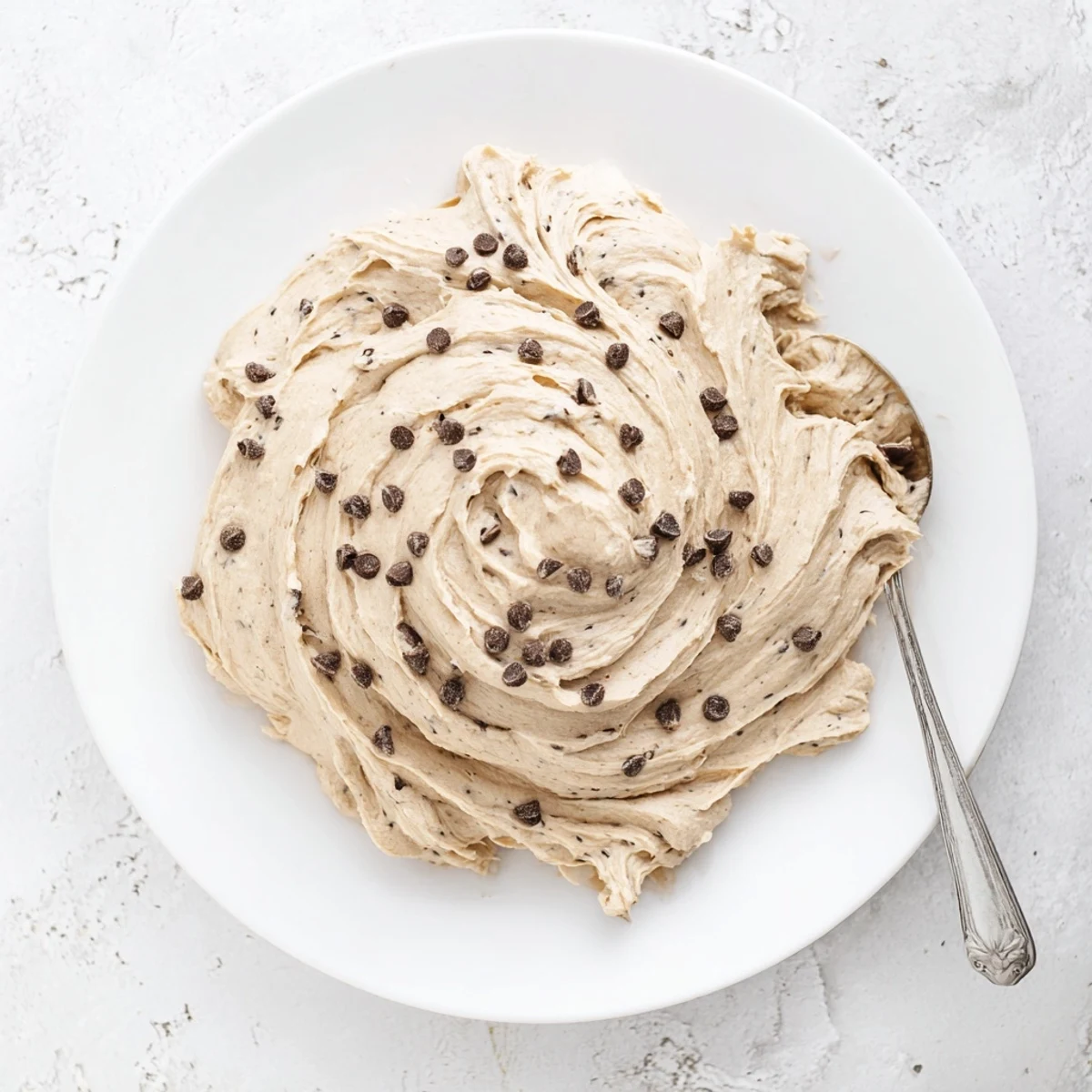 Glossy Cookie Dough Frosting is piped onto chocolate cupcakes, creating a rich dessert topping.