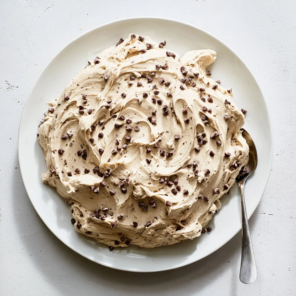 Spatula lifting Cookie Dough Frosting from a mixing bowl, showing a thick, dough-like texture.