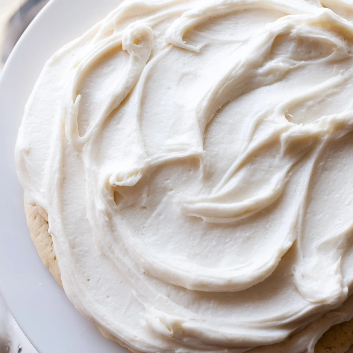 Bright white Easy Sugar Cookie Frosting being spread smoothly over a round sugar cookie.