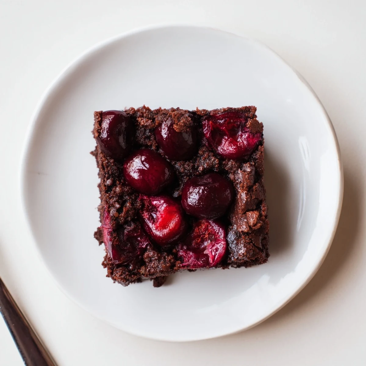 A slice of Roasted Cherry Brownies reveals juicy cherries and a moist crumb, served on a white plate.  