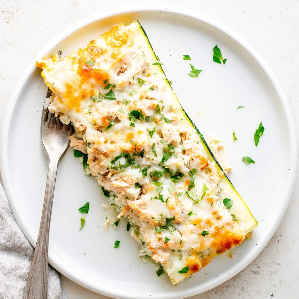 Sliced layers of Chicken Alfredo Zucchini Lasagna show tender chicken and fresh zucchini ribbons in a casserole dish.