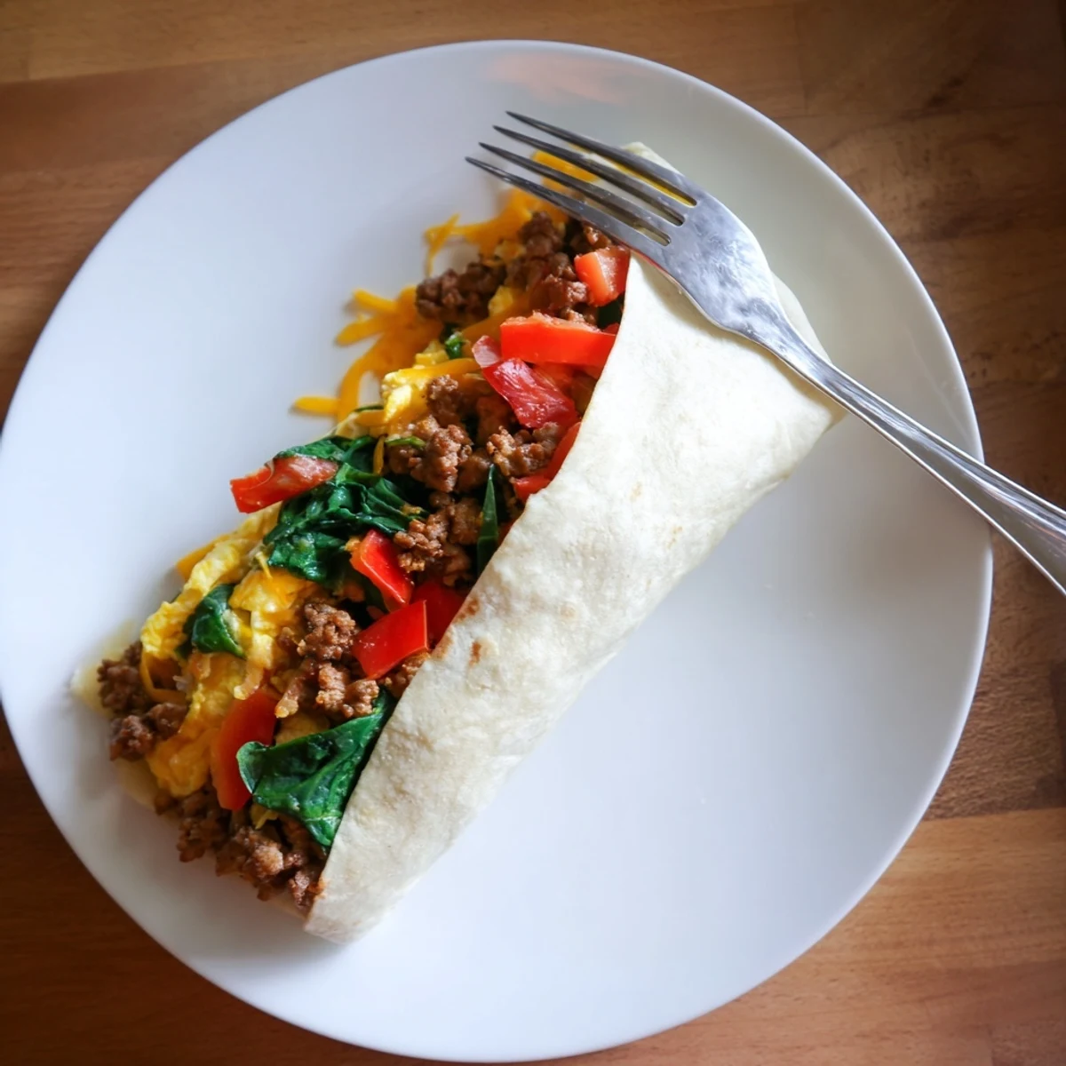 Sliced make-ahead breakfast burritos revealing colorful layers of eggs, vegetables, sausage, and shredded cheese inside