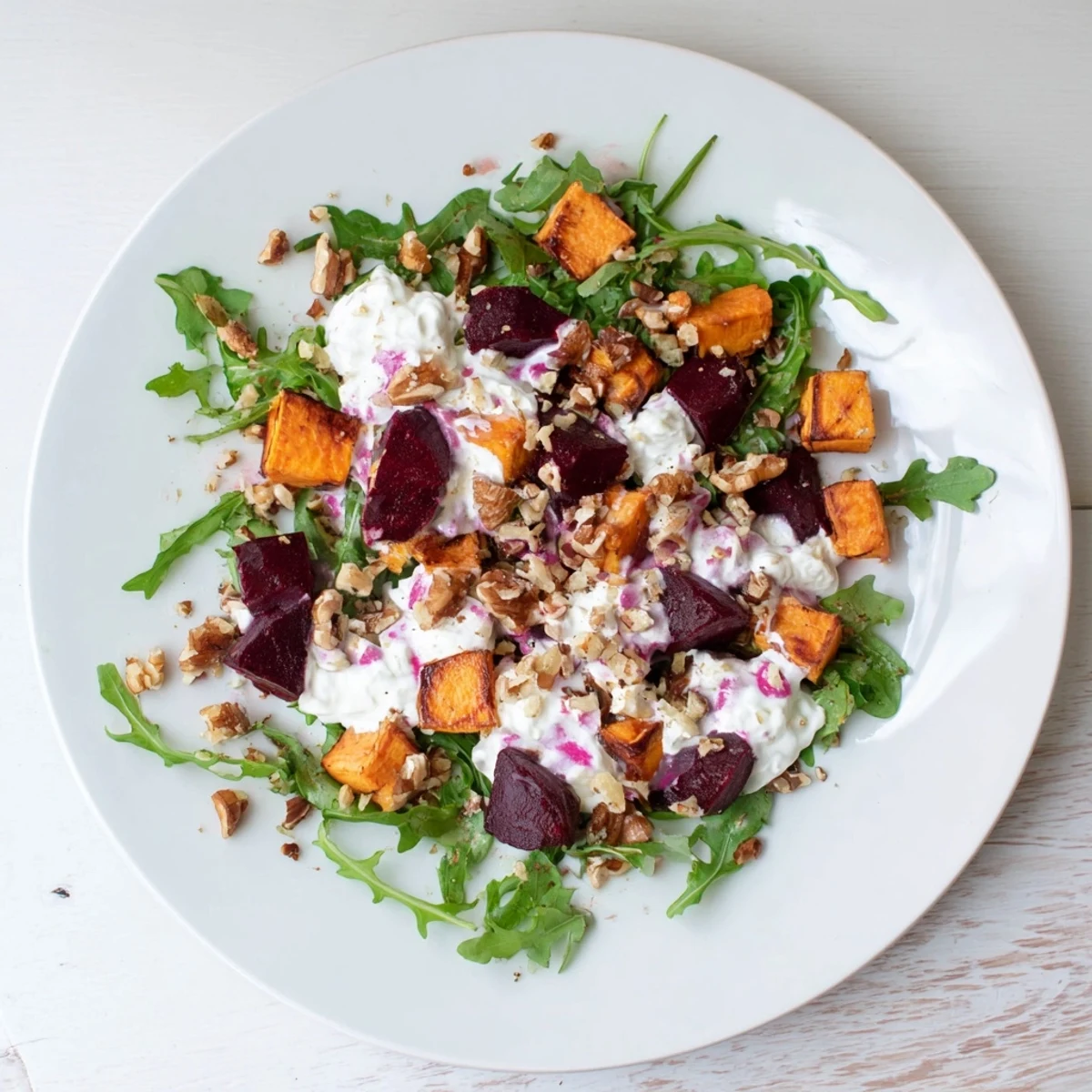 Golden roasted beets and sweet potatoes topped with crumbled feta and creamy yogurt dressing on a bed of fresh greens