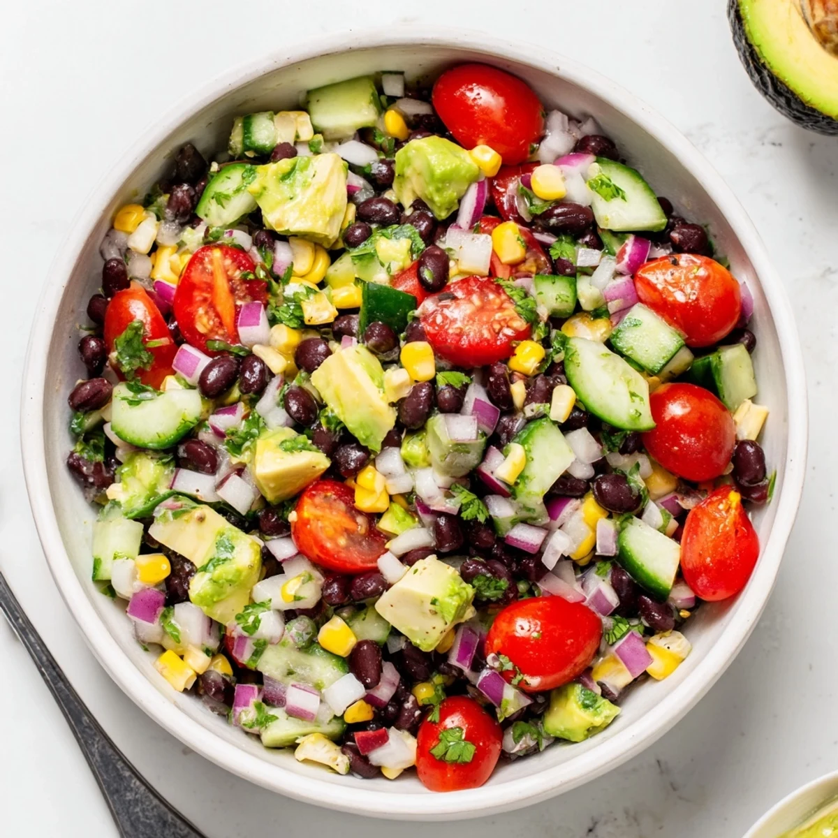 Colorful chopped black bean salad with fresh vegetables, creamy avocado, and zesty lime dressing in a white bowl
