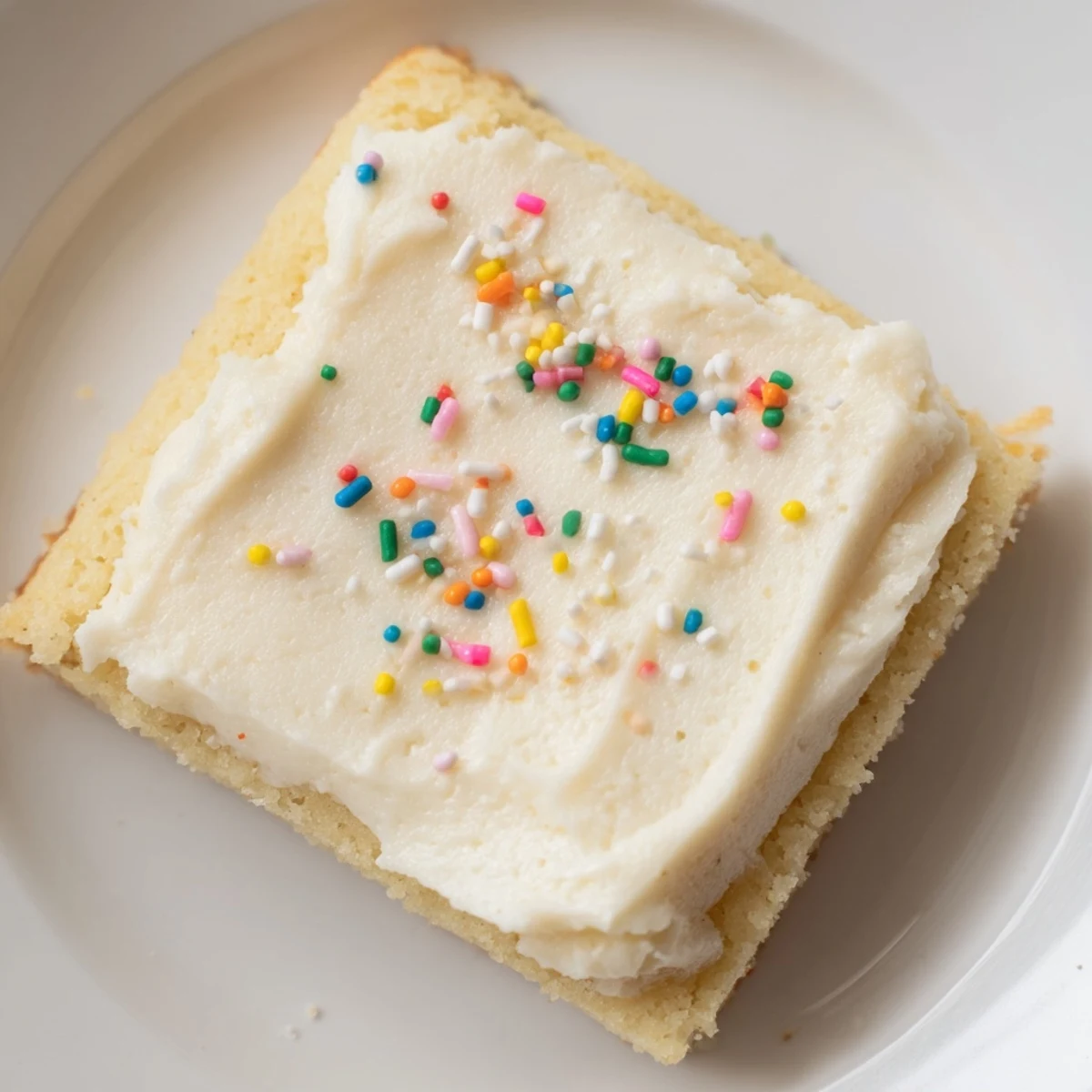 Golden sugar cookie bars with thick vanilla frosting and festive sprinkles for parties