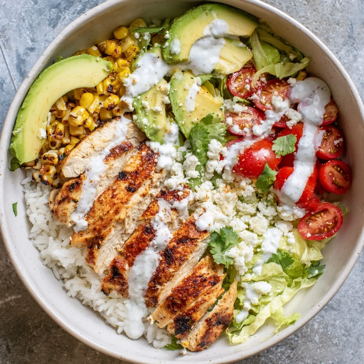 Hearty Mexican-inspired street corn chicken bowl topped with juicy grilled chicken breast, charred corn kernels, creamy avocado, crumbled cotija, and tangy lime crema