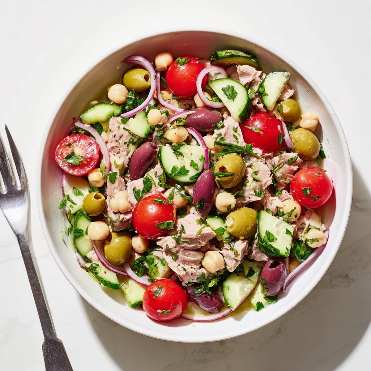 Colorful hearty tuna and garbanzo bean salad bowl with fresh vegetables and zesty lemon dressing drizzled on top