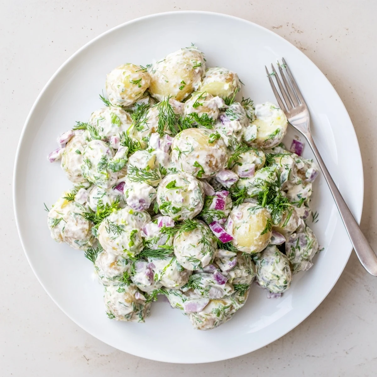 Light and tangy Greek yogurt potato salad featuring red onions, dill, and parsley on a white platter