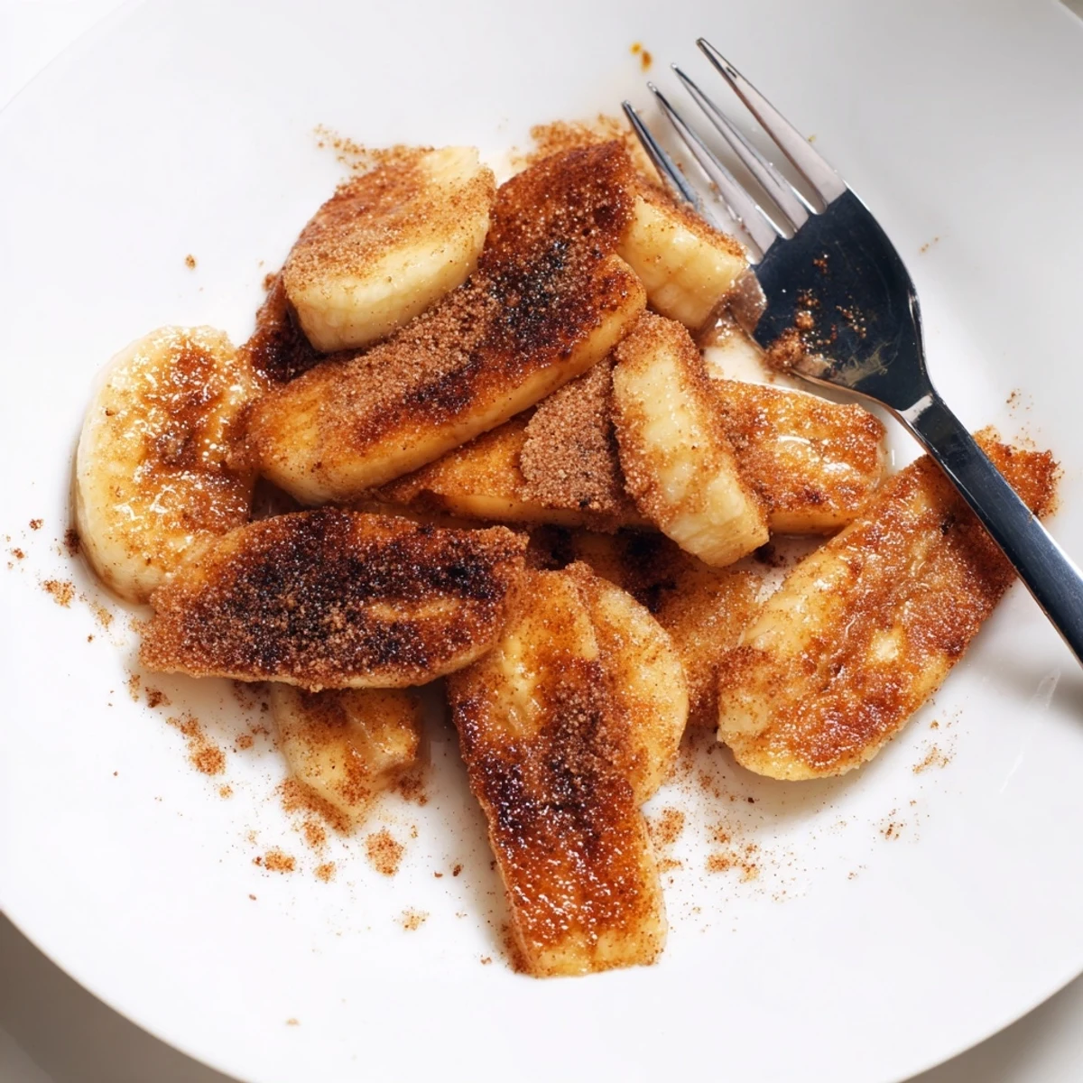 Golden pan fried cinnamon bananas caramelized in butter with brown sugar dusting on warm skillet