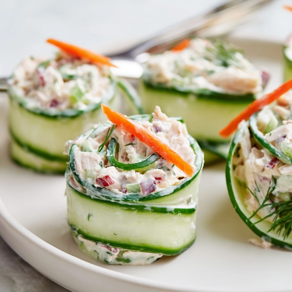 Fresh chicken salad cucumber roll ups on a white platter with vibrant green ribbons
