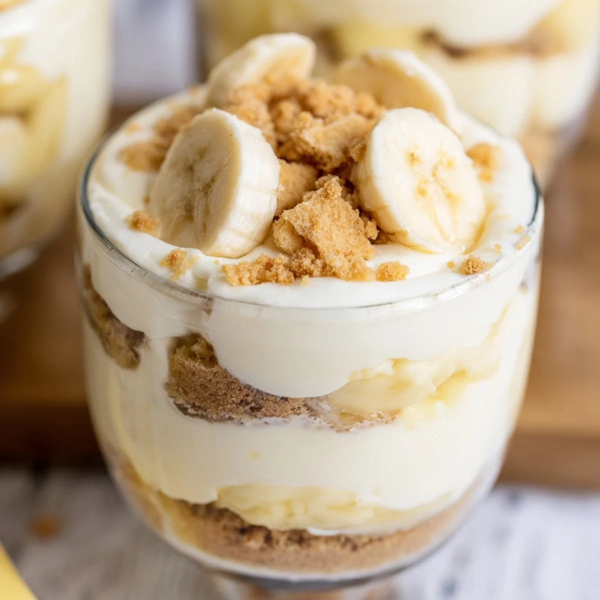 Creamy no bake banana pudding cheesecake cups topped with fresh banana slices and vanilla wafer crumbs