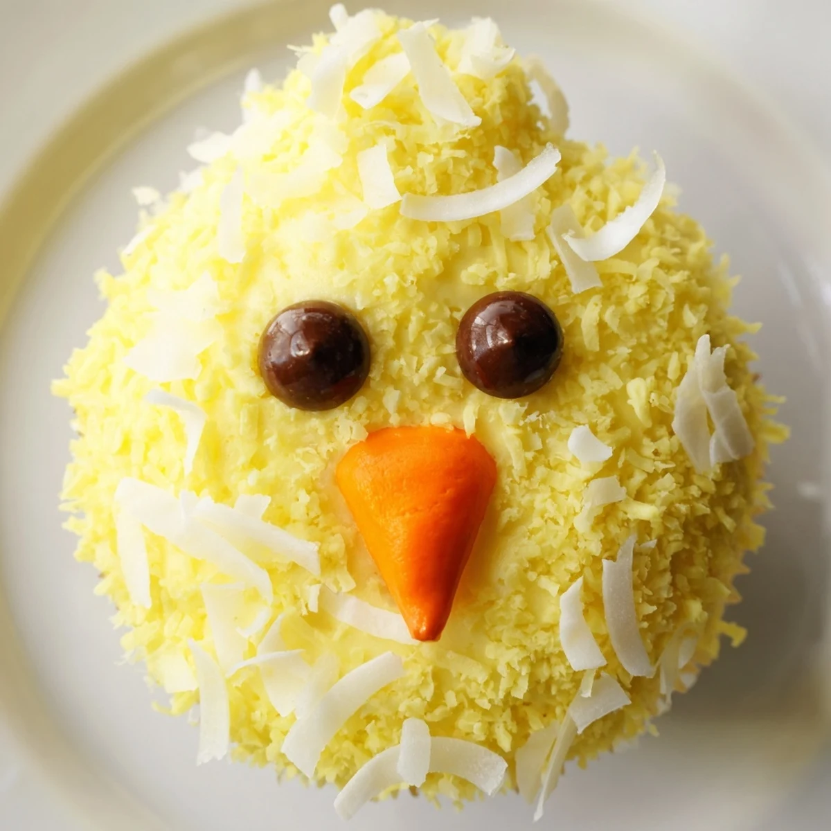 Bright yellow buttercream Easter Chick Cupcakes decorated with chocolate chip eyes and orange candy beaks ready to serve