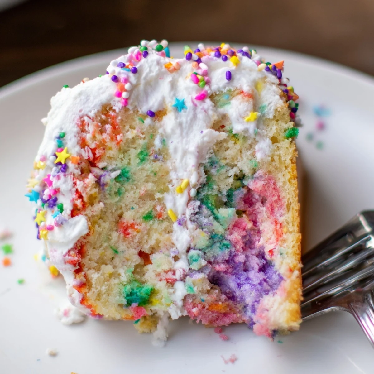 Unicorn Poke Cake topped with colorful sprinkles, served on a white plate for parties.