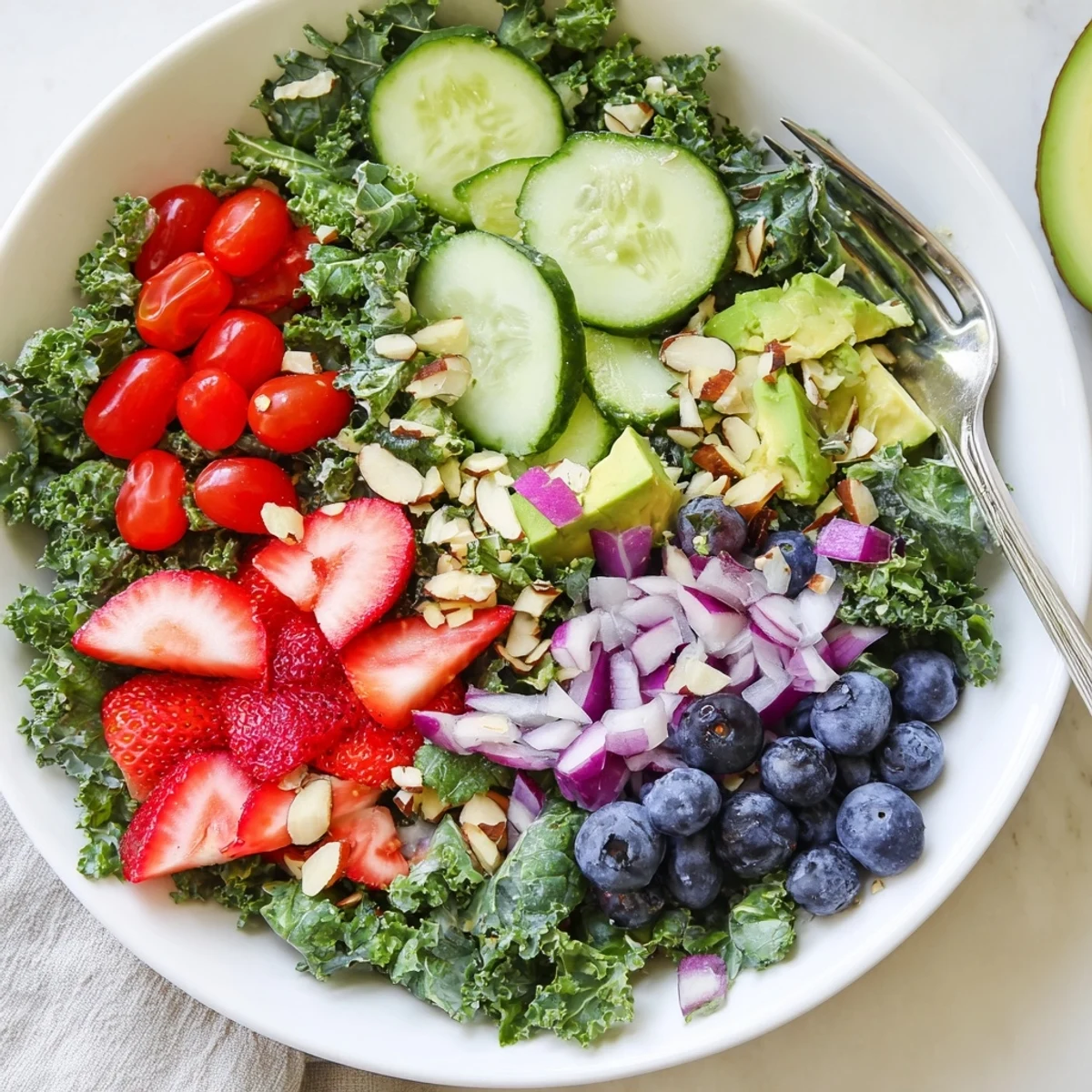 A colorful summer kale salad topped with fresh berries, feta, and toasted almonds