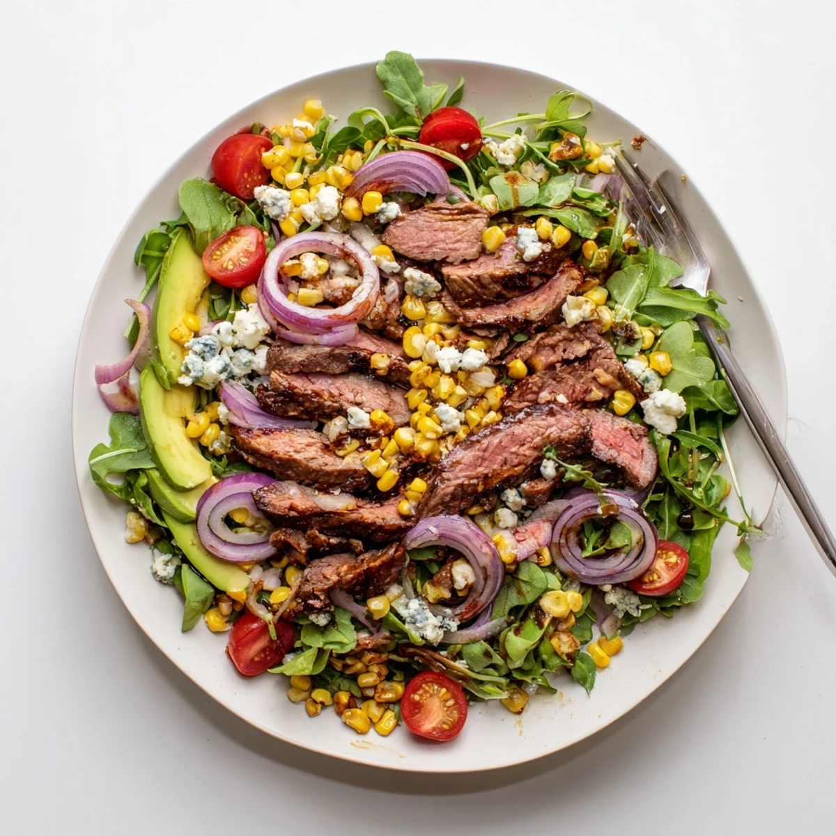 Sliced balsamic steak gorgonzola salad with charred corn on a white platter