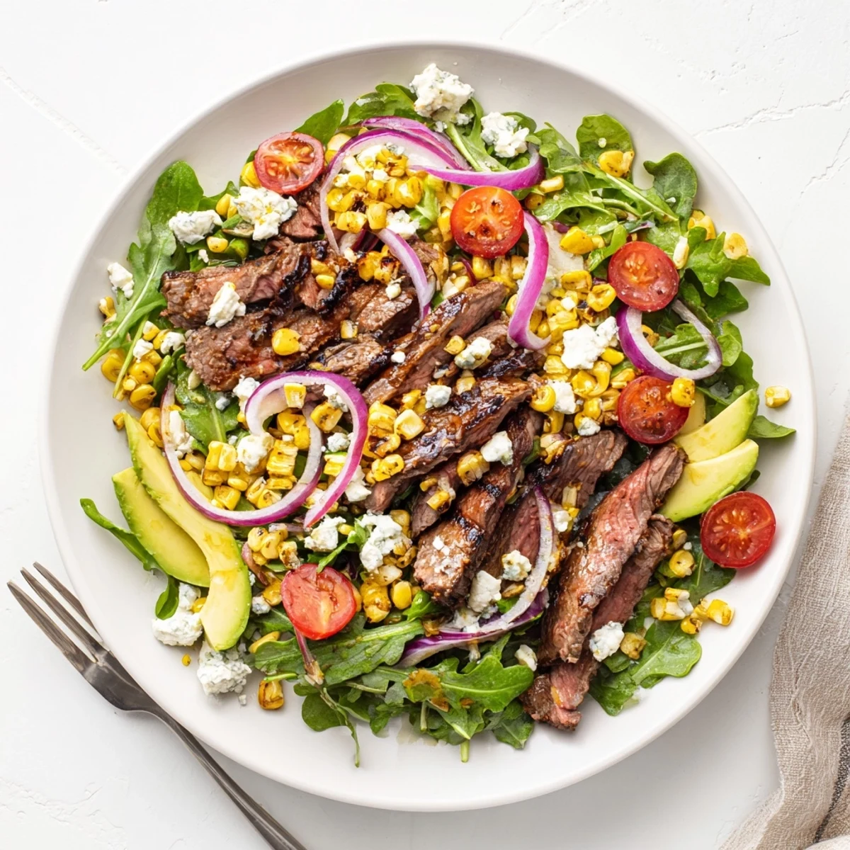 Balsamic steak gorgonzola salad drizzled with vinaigrette beside halved cherry tomatoes and avocado