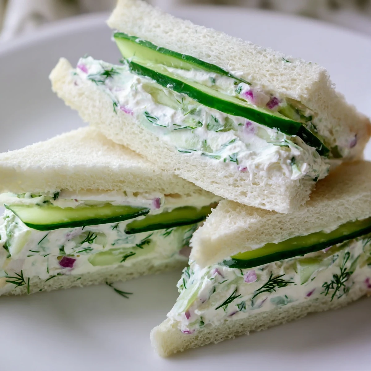 Creamy cucumber salad sandwiches with thinly sliced English cucumbers and red onion on bread, served as refreshing vegetarian finger food
