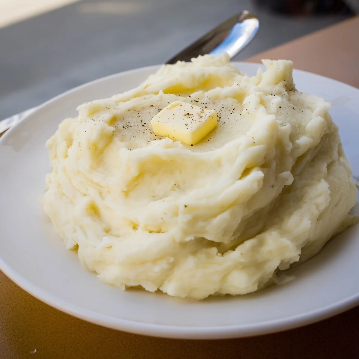 Smooth velvety mashed potatoes scooped onto a plate beside roasted holiday turkey