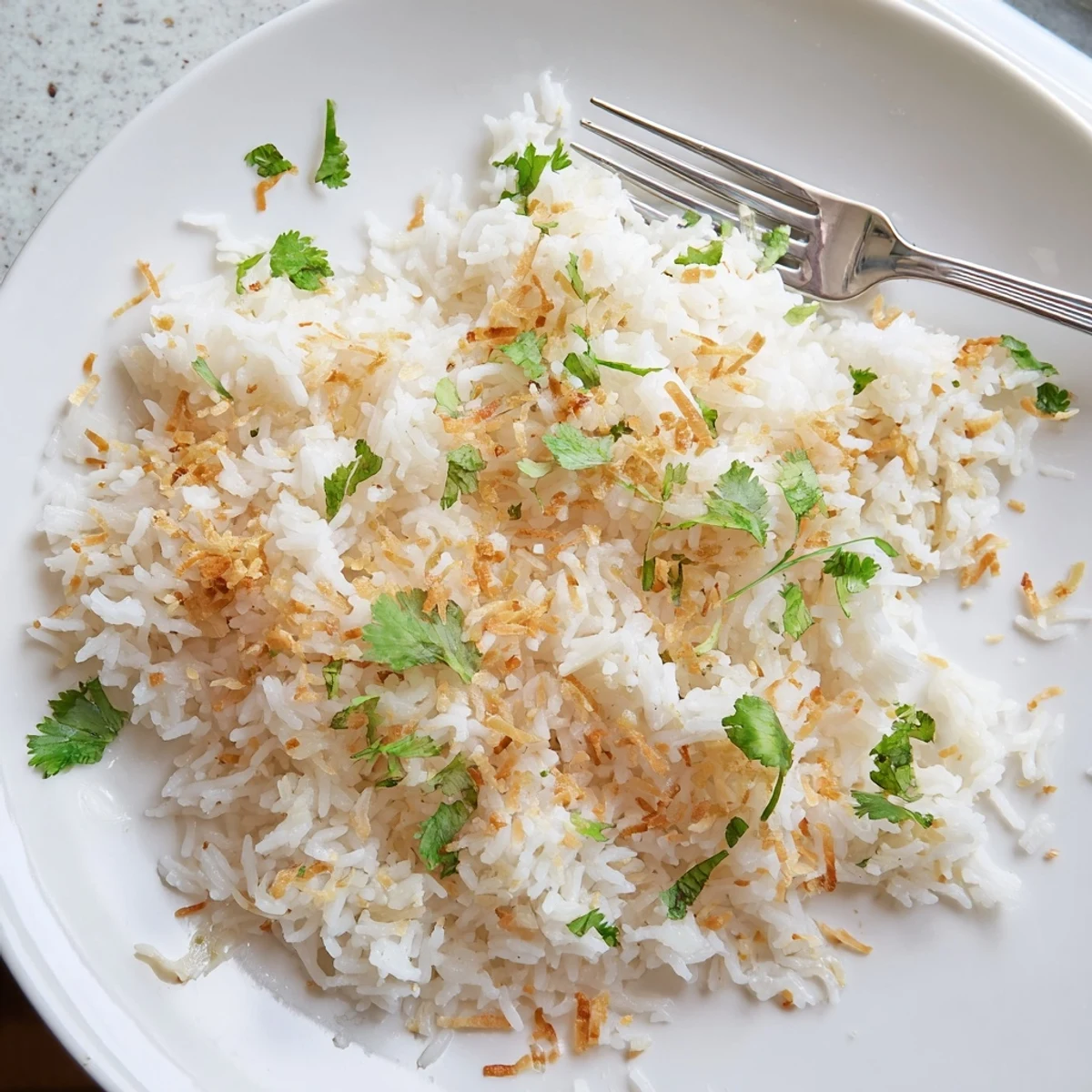Steaming bowl of fragrant coconut rice topped with golden toasted coconut and scattered cilantro leaves
