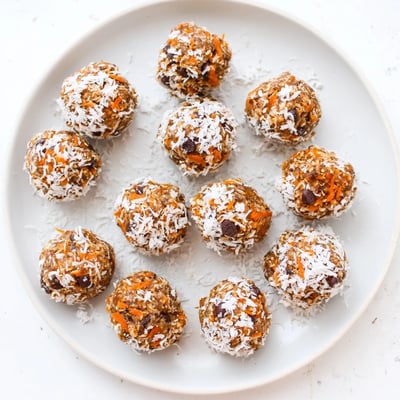 A close-up of No Bake Carrot Cake Bites reveals moist, textured interiors packed with oats, dates, and warm spices on a white marble surface.