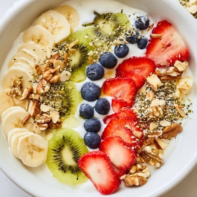 A glass of green tea sits beside the Healthy Breakfast Bowl with crunchy granola and sliced bananas.