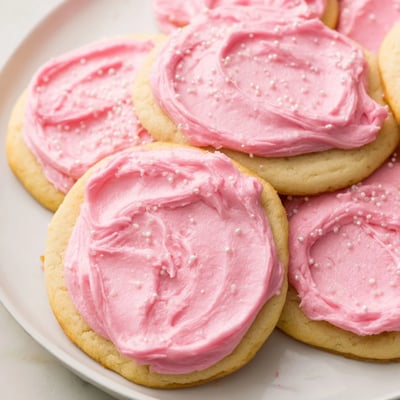 Thick Crumbl Sugar Cookies on a wire rack, showing soft centers and vibrant pink almond frosting swirls.