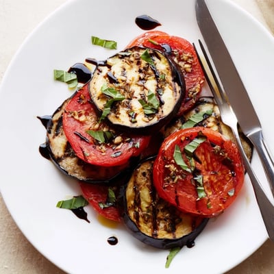 Tender grilled tomato eggplant drizzled with balsamic glaze and fresh basil